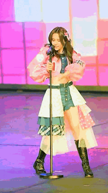 a woman in a pink jacket is singing into a microphone on stage