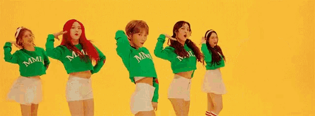 a group of women are standing next to each other on a yellow background wearing green sweaters and skirts .