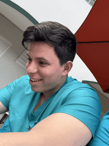 a young man wearing a blue scrub top smiles in front of an umbrella
