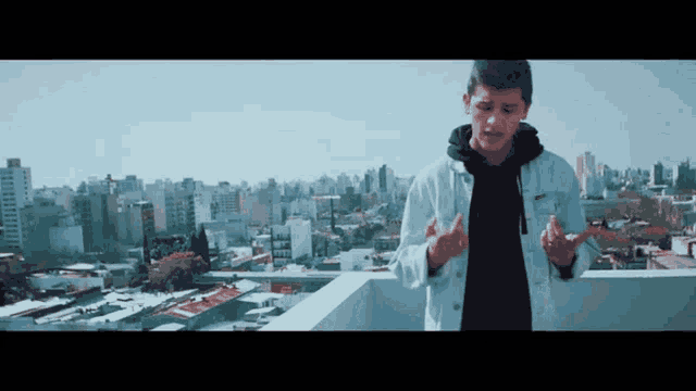 a man in a white jacket is standing on a rooftop overlooking a city