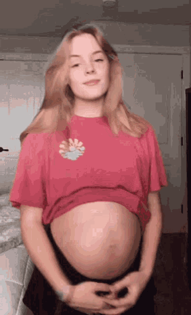 a pregnant woman in a pink shirt is holding her belly and smiling .