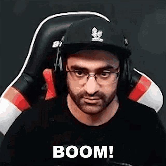 a man wearing a hat and headphones is sitting in a chair and says boom .