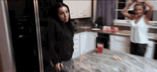 two women are standing in a kitchen and one is holding a red cup .