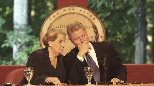 a man and a woman sitting at a table with glasses of water in front of a seal that says the nyc river