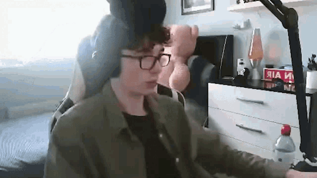 a young man wearing glasses and headphones is sitting in a chair in front of a microphone .