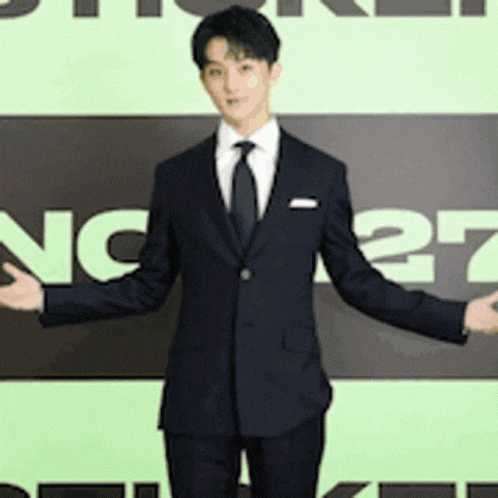 a man in a suit and tie is standing in front of a sign with the number 27 on it .
