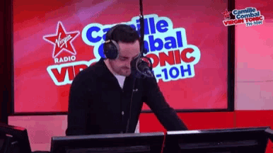 a man wearing headphones is standing in front of a virgin radio sign