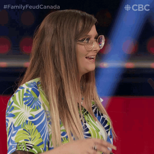 a woman wearing glasses and a blue and green shirt with the words family feud canada behind her