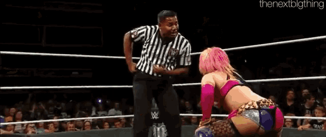a referee is standing in the middle of a wrestling ring with two women wrestling .