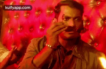 a man with a mustache is sitting on a red leather couch and smoking a cigarette .