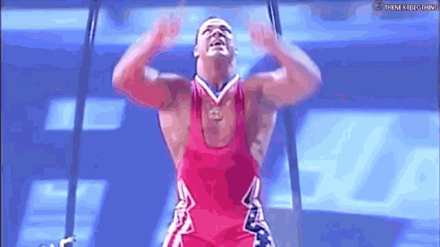 a man in a red and white tank top is doing a handstand on a bar .