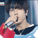 a young man is singing into a microphone while wearing a red and blue sweater .