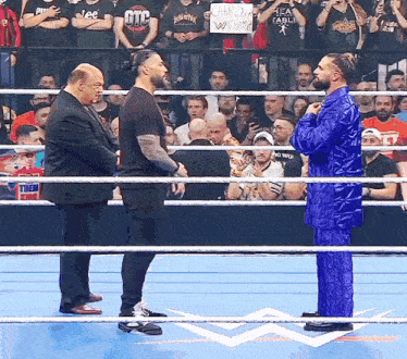 a man in a blue suit stands in the middle of a wrestling ring with two other men