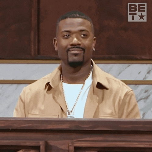 a man with a beard is sitting at a podium in front of a sign that says be