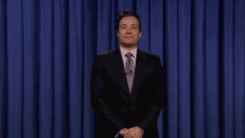 a man in a suit and tie is standing in front of a blue curtain in a room .
