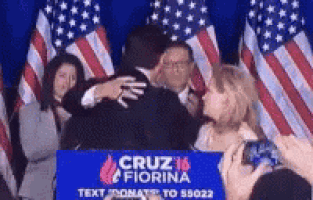 a man is hugging another man in front of a sign that says cruz fiorina