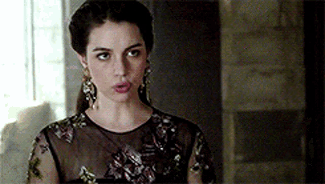 a woman in a black dress and earrings is standing in a room .