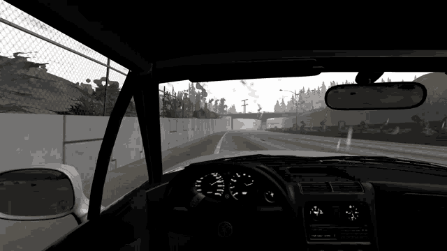 a car is driving down a highway with a fence in the background and a rear view mirror