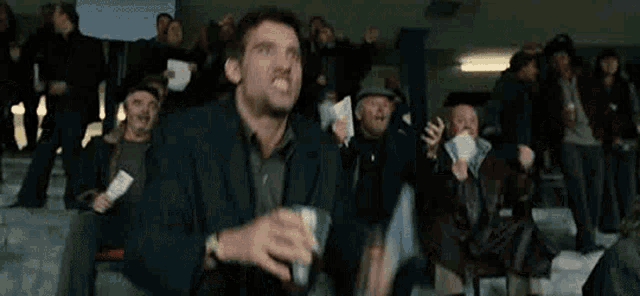 a man is holding a cup of beer and a newspaper in front of a crowd .