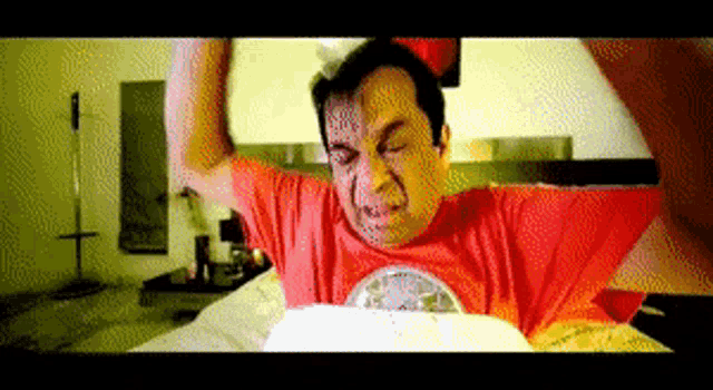 a man in a red shirt is sitting on a bed with his arms outstretched