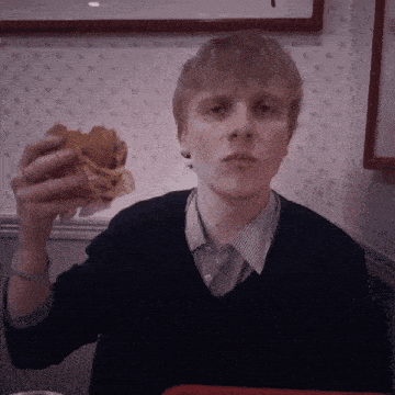 a young man is eating a hamburger with a ring on his finger