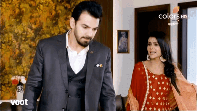a man in a suit stands next to a woman in a red dress on a tv screen that says voot