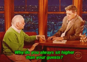 a man in a green sweater is sitting at a table talking to another man