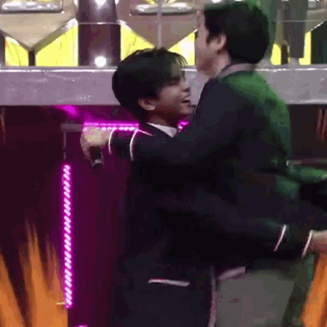 a couple of men are hugging each other on a stage in front of a microphone .