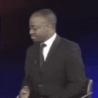 a man in a white suit and pink tie is sitting in a chair .