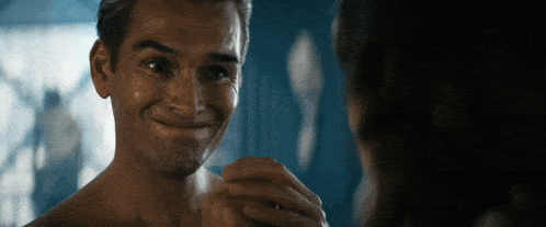 a shirtless man is looking at himself in the mirror and smiling