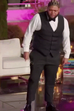 a man wearing a tuxedo and a crown is standing in front of a chair