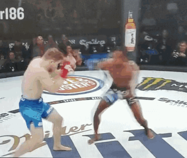 two men are fighting in a ring with a monster energy drink advertisement on the wall behind them