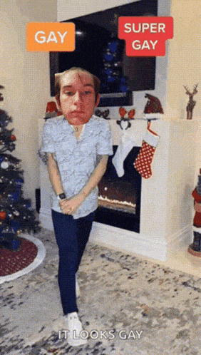 a man is standing in front of a fireplace and a christmas tree with a super gay sticker on his face