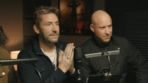 two men are sitting in front of microphones with their hands folded