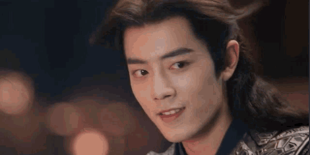 a close up of a young man with long hair and a ponytail looking at the camera .