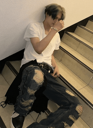 a young man sitting on a set of stairs wearing ripped jeans