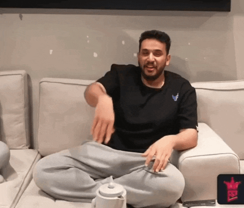 a man is sitting on a couch with his legs crossed and a teapot in front of him with a crown on it