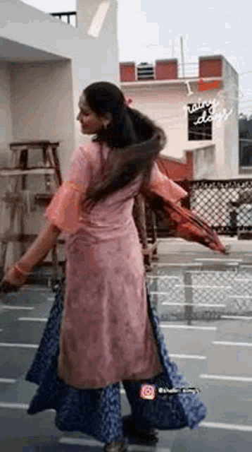 a woman in a pink dress and blue skirt is dancing on a rooftop .