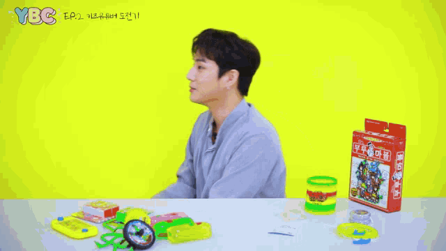 a young man is sitting at a table with toys and a box that says ' ybc ' on it