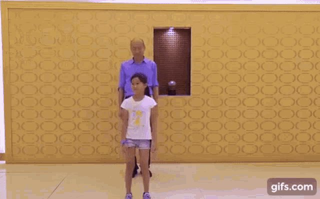 a man and a little girl are dancing in front of a wall with chinese characters