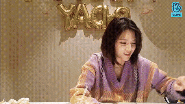 a woman is sitting at a table with balloons on the wall behind her .