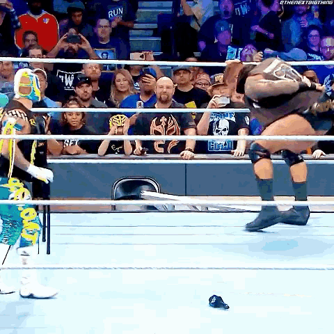 a wrestler is jumping over a rope while another wrestler looks on ..