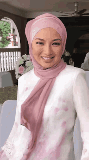 a woman wearing a pink hijab and a white shirt smiles at the camera