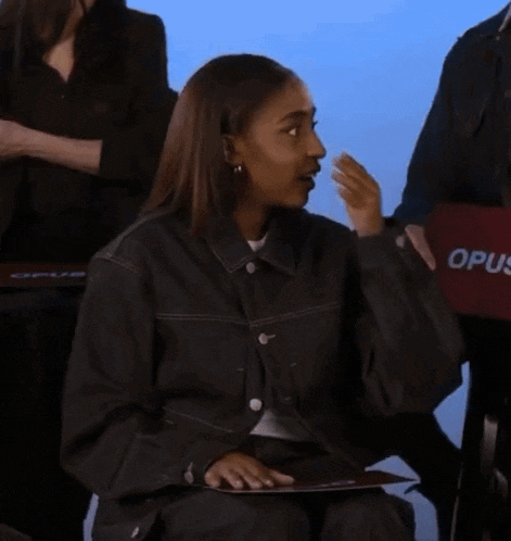a woman in a black jacket is covering her face while holding a sign that says opus