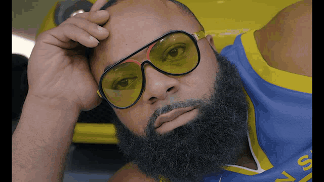 a man with a beard wearing yellow sunglasses and a golden state warriors shirt