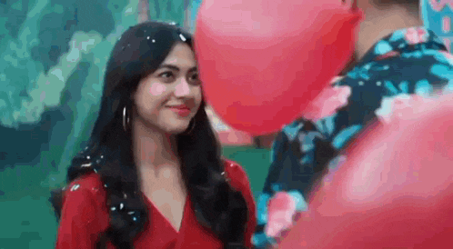 a woman in a red dress is looking at a man with a red balloon in front of her .