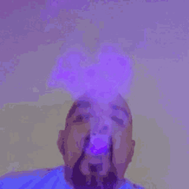 a man with a beard is blowing purple smoke into the air .