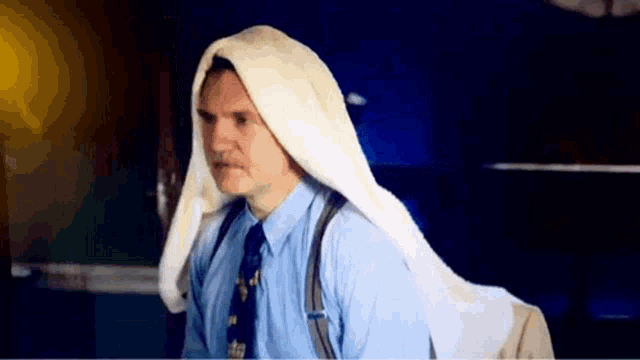 a man in a blue shirt and tie has a white towel on his head .