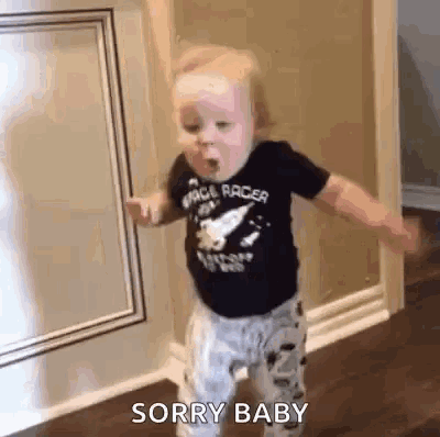 a baby is standing in a room and making a funny face while wearing a space racer shirt .
