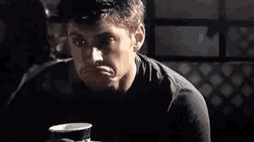 a man is sitting at a table with a cup of coffee in his hand .
